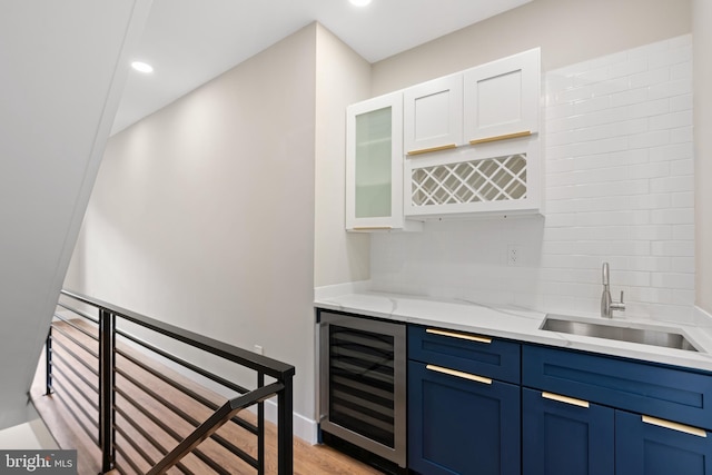 bar featuring light stone countertops, light wood-type flooring, sink, white cabinets, and wine cooler