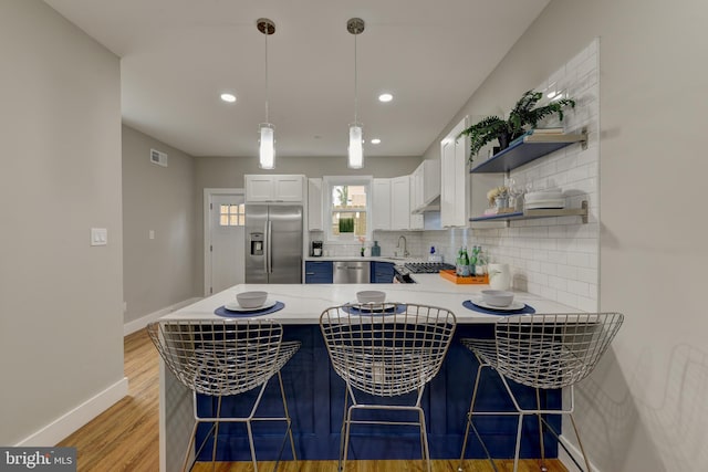 kitchen with white cabinetry, kitchen peninsula, decorative light fixtures, a breakfast bar area, and appliances with stainless steel finishes