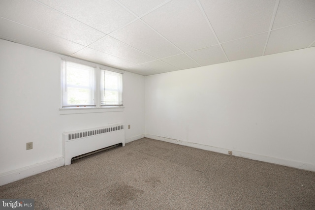 carpeted empty room with radiator and a paneled ceiling