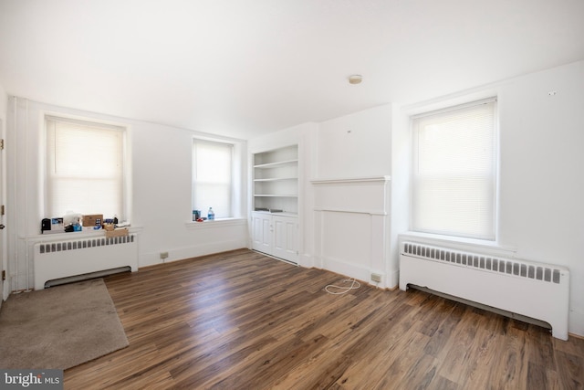 unfurnished living room with a wealth of natural light, dark hardwood / wood-style flooring, and radiator heating unit