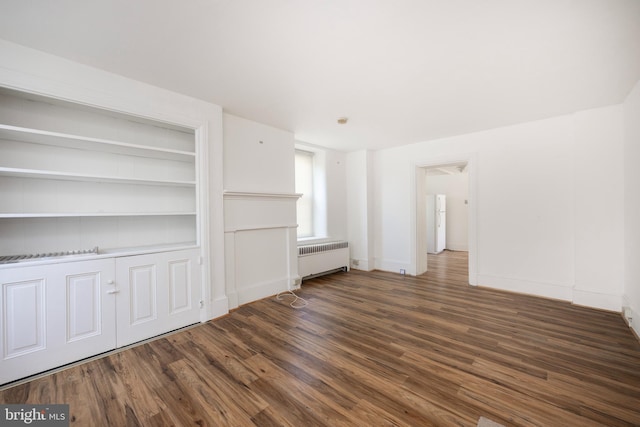 unfurnished living room featuring built in shelves, dark hardwood / wood-style floors, and radiator