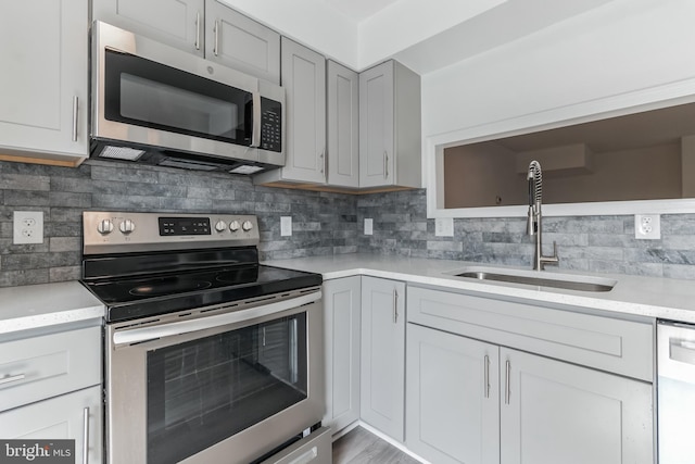 kitchen featuring decorative backsplash, stainless steel appliances, gray cabinetry, and sink