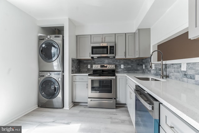 kitchen with decorative backsplash, appliances with stainless steel finishes, sink, gray cabinets, and stacked washer and dryer