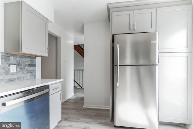 kitchen with beamed ceiling, light wood-type flooring, backsplash, and appliances with stainless steel finishes