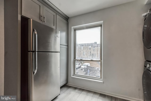 kitchen with gray cabinetry, stainless steel fridge, light hardwood / wood-style flooring, and stacked washer / drying machine