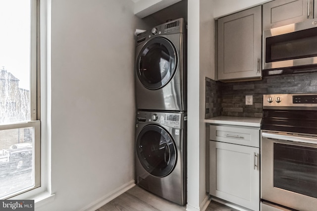 clothes washing area featuring light wood-type flooring and stacked washing maching and dryer