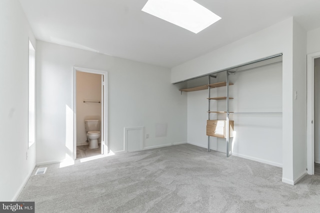 unfurnished bedroom with ensuite bath, a skylight, a closet, and light colored carpet