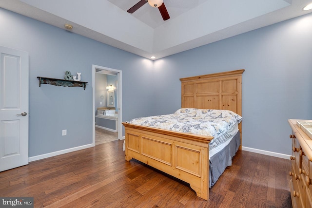 bedroom with a tray ceiling, ensuite bath, dark wood-type flooring, and ceiling fan