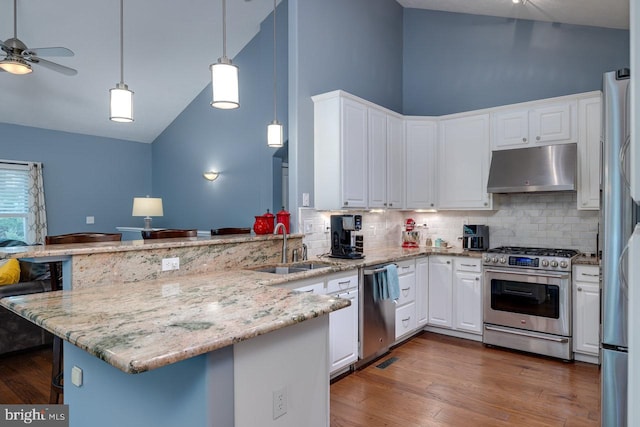 kitchen with appliances with stainless steel finishes, high vaulted ceiling, kitchen peninsula, and hardwood / wood-style floors