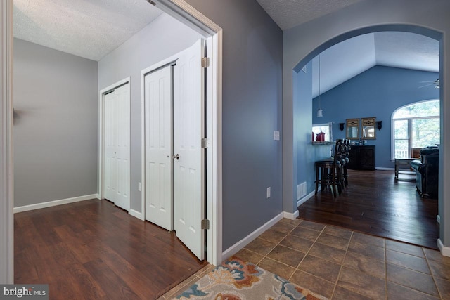 hallway with a textured ceiling, dark tile patterned floors, and vaulted ceiling