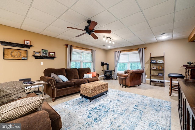 tiled living room featuring a wood stove, ceiling fan, a paneled ceiling, and track lighting