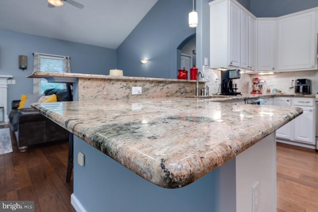 kitchen featuring white cabinetry, pendant lighting, hardwood / wood-style floors, lofted ceiling, and backsplash