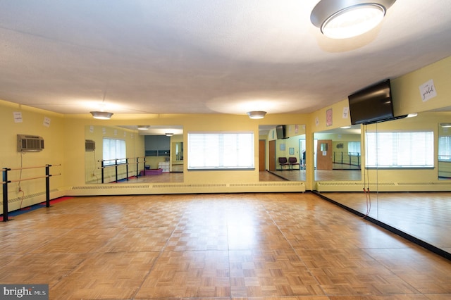 exercise room featuring parquet flooring, a wall mounted air conditioner, baseboard heating, and a healthy amount of sunlight