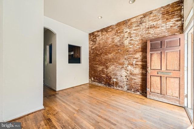 empty room featuring wood-type flooring and brick wall