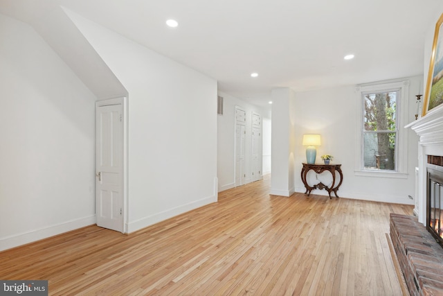 unfurnished room featuring a fireplace, light hardwood / wood-style flooring, and vaulted ceiling