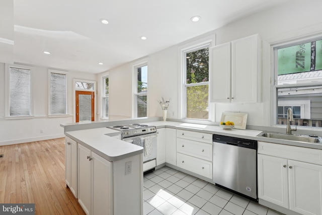 kitchen with sink, kitchen peninsula, stainless steel dishwasher, light wood-type flooring, and white gas range