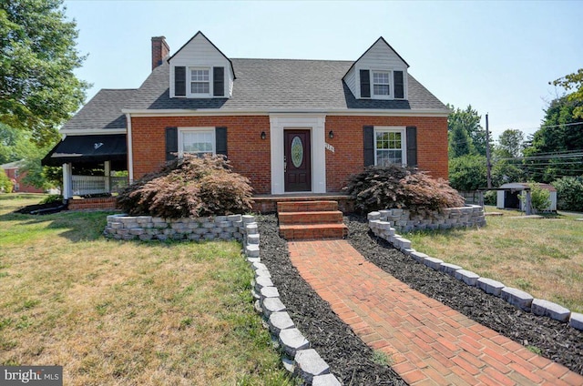 cape cod-style house featuring a front lawn and a storage unit