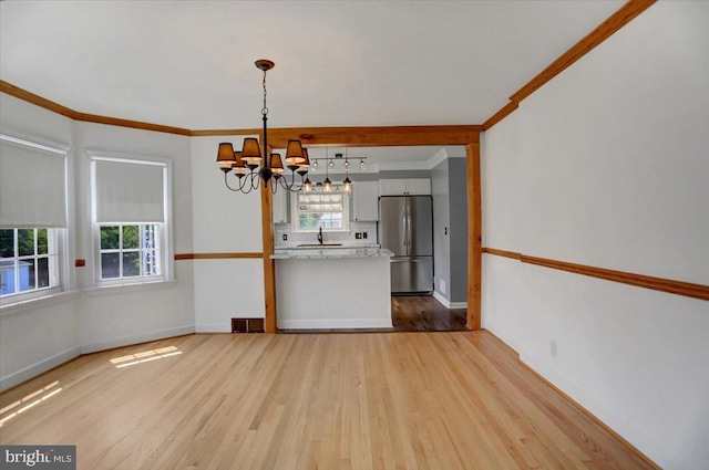 unfurnished dining area with ornamental molding, sink, light hardwood / wood-style floors, and a notable chandelier