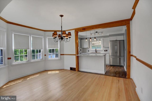 kitchen with an inviting chandelier, stainless steel fridge, tasteful backsplash, light wood-type flooring, and hanging light fixtures