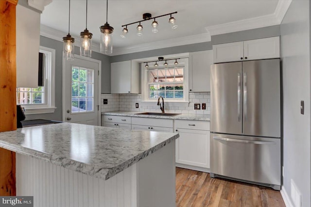 kitchen featuring pendant lighting, decorative backsplash, sink, stainless steel refrigerator, and white cabinets