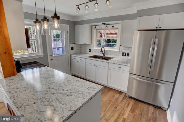 kitchen with white cabinetry, stainless steel refrigerator, hanging light fixtures, light stone countertops, and sink