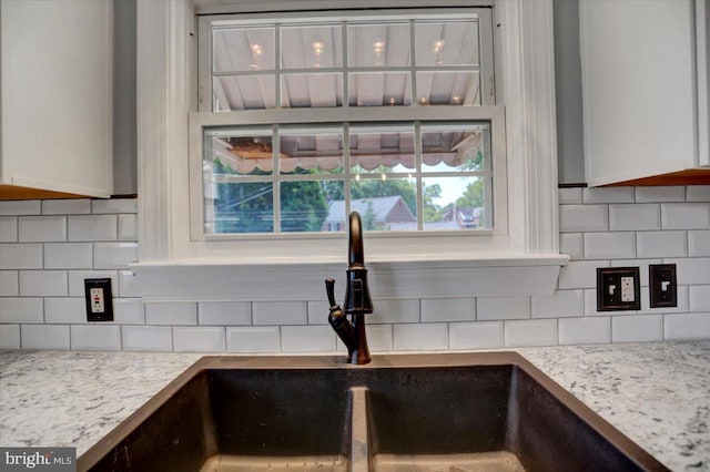 details featuring decorative backsplash, white cabinets, light stone counters, and sink