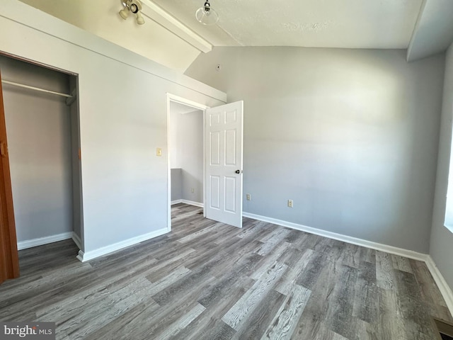 unfurnished bedroom with hardwood / wood-style flooring, lofted ceiling with beams, and a closet