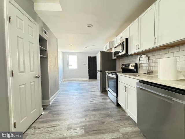 kitchen featuring light wood-type flooring, tasteful backsplash, stainless steel appliances, sink, and white cabinets