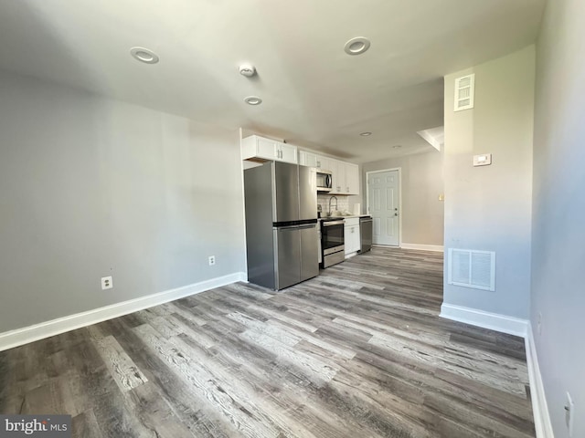 kitchen with appliances with stainless steel finishes, light wood-type flooring, tasteful backsplash, and white cabinetry