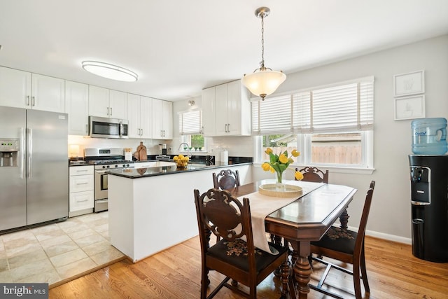 kitchen with decorative light fixtures, light hardwood / wood-style floors, white cabinetry, and appliances with stainless steel finishes