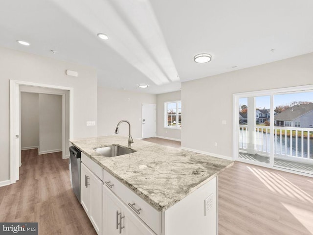 kitchen with light stone countertops, sink, a water view, a center island with sink, and white cabinets