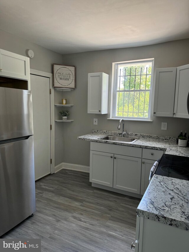 kitchen featuring hardwood / wood-style floors, white cabinetry, sink, light stone counters, and stainless steel fridge