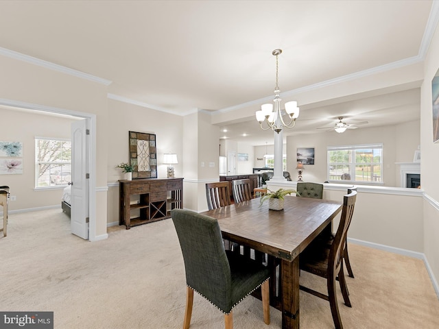 carpeted dining space featuring ceiling fan with notable chandelier, a healthy amount of sunlight, ornate columns, and crown molding