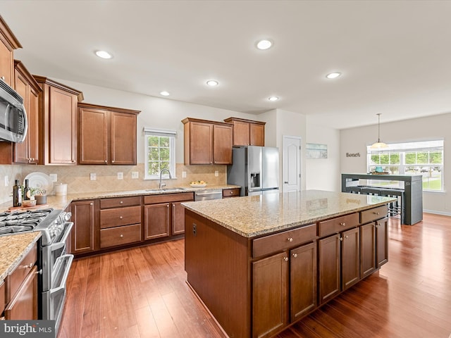 kitchen with stainless steel appliances, sink, pendant lighting, hardwood / wood-style floors, and a kitchen island