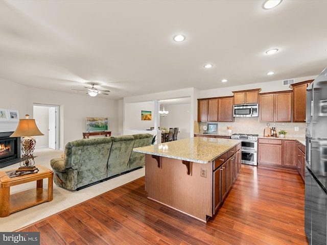 kitchen with a kitchen bar, backsplash, ceiling fan with notable chandelier, stainless steel appliances, and a kitchen island