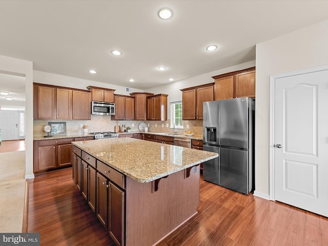 kitchen with light stone counters, a breakfast bar, stainless steel appliances, dark wood-type flooring, and a kitchen island