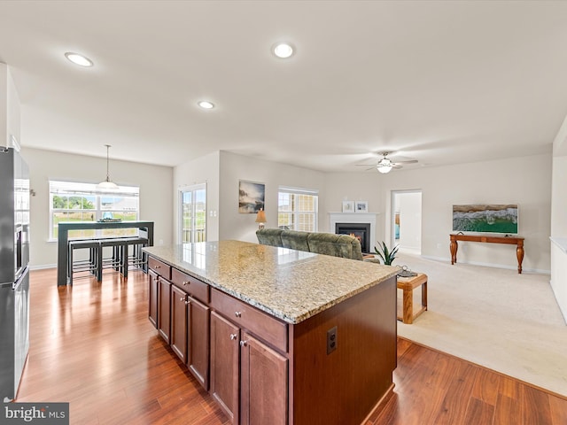 kitchen with ceiling fan, hanging light fixtures, light stone counters, hardwood / wood-style floors, and a kitchen island