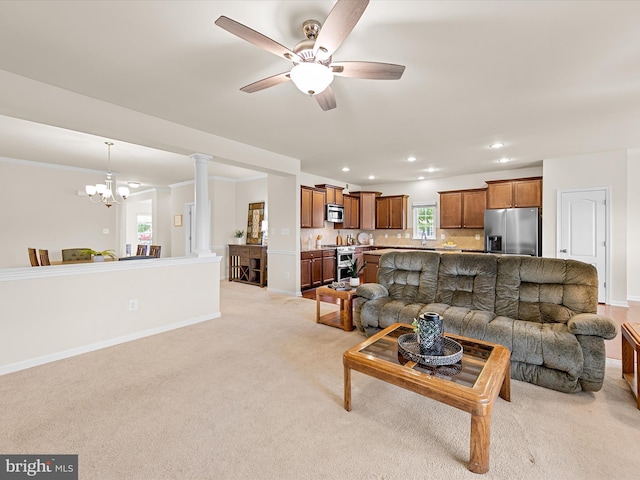 carpeted living room with ceiling fan with notable chandelier and ornate columns