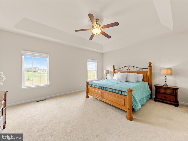 carpeted bedroom with a raised ceiling and ceiling fan