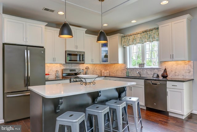 kitchen featuring backsplash, dark wood-type flooring, a kitchen island, stainless steel appliances, and decorative light fixtures