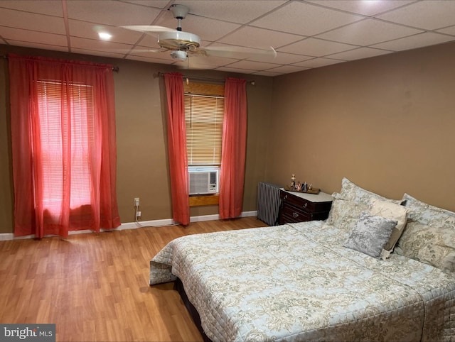 bedroom with hardwood / wood-style floors, cooling unit, a drop ceiling, radiator heating unit, and ceiling fan