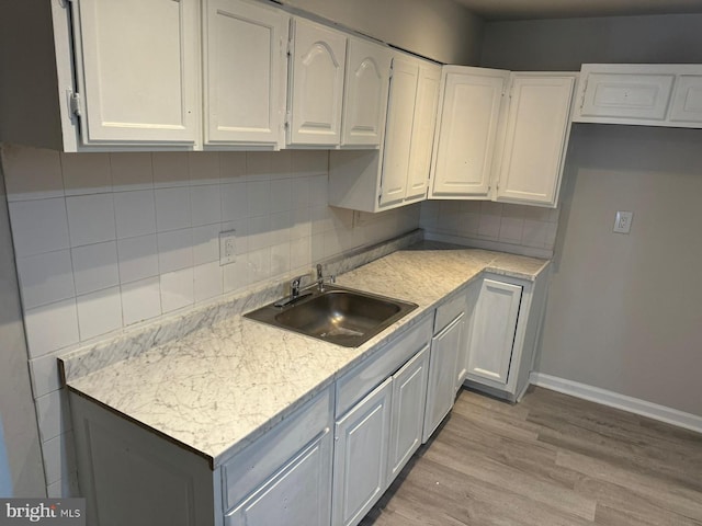 kitchen featuring sink, decorative backsplash, light hardwood / wood-style floors, light stone counters, and white cabinetry