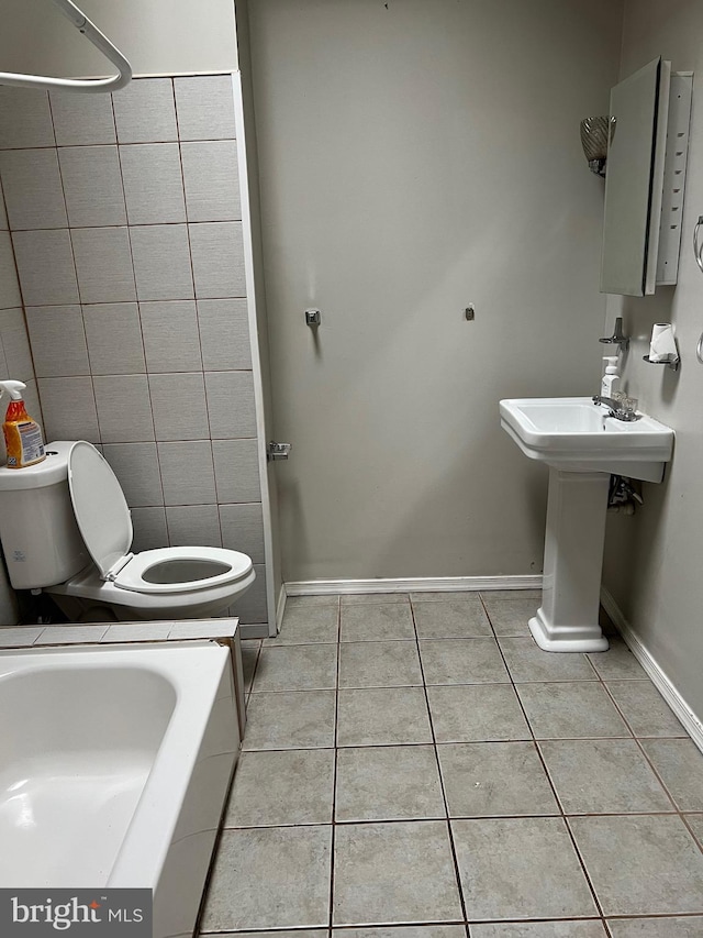 bathroom featuring a bathtub, tile patterned floors, sink, toilet, and tile walls