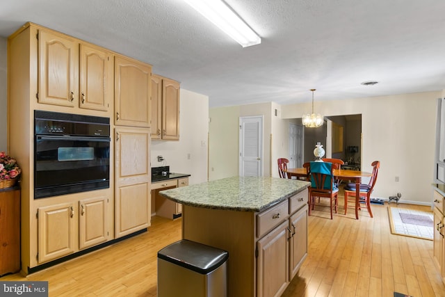 kitchen with decorative light fixtures, a notable chandelier, oven, a kitchen island, and light wood-type flooring