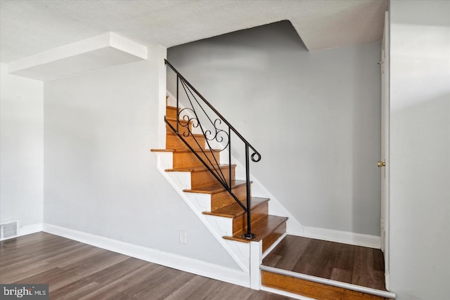 stairs with wood-type flooring and a textured ceiling