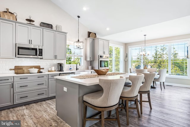 kitchen featuring gray cabinetry, stainless steel appliances, pendant lighting, vaulted ceiling, and a kitchen island