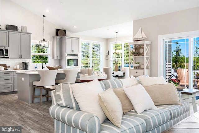 living room with an inviting chandelier, vaulted ceiling, and light wood-type flooring