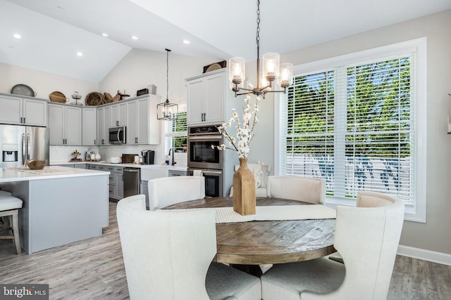 dining room with an inviting chandelier, vaulted ceiling, and light wood-type flooring