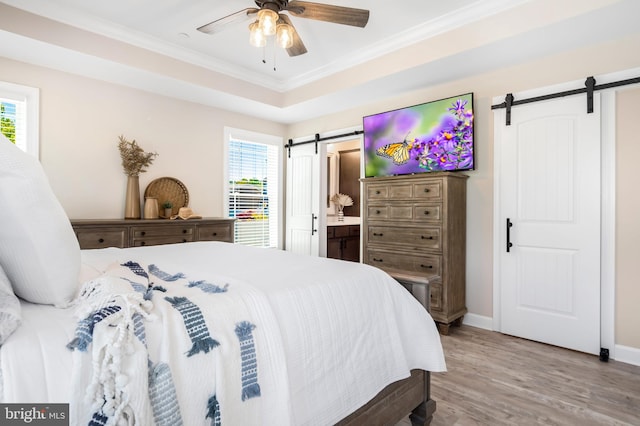 bedroom with ensuite bath, ceiling fan, a barn door, a tray ceiling, and wood-type flooring