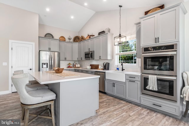 kitchen with appliances with stainless steel finishes, gray cabinetry, sink, a center island, and hanging light fixtures